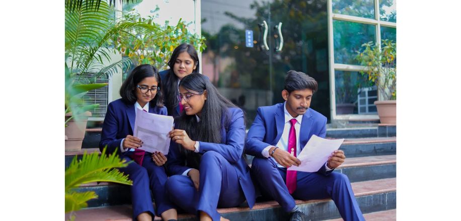 Four students wearing uniform, sitting on the stairs and checking their gmat or gre scores on a paper